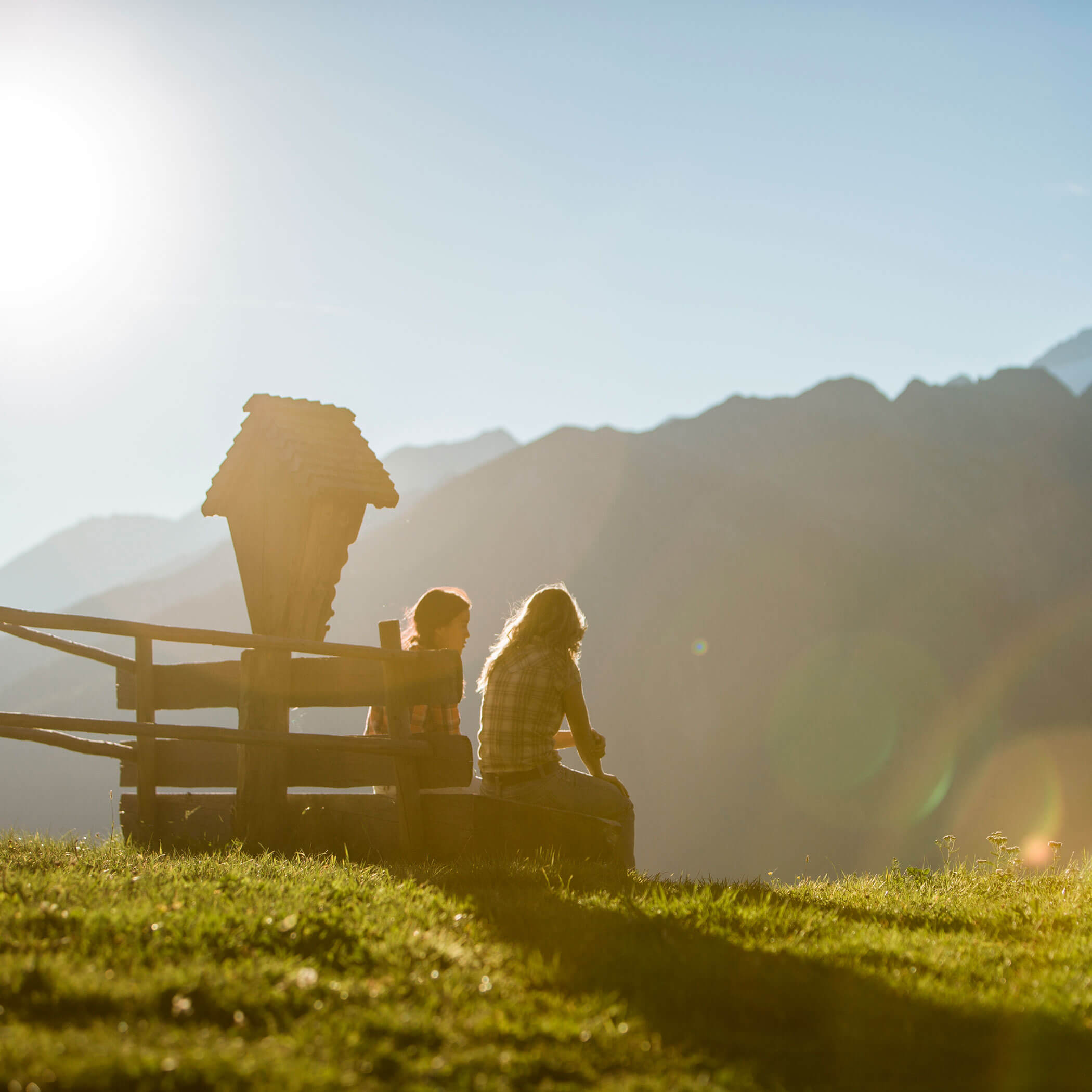 Mutter und Tochter sitzen auf einer Rastbank im Sommer und genießen den Ausblick in die Berge - Hotel Mühlwald