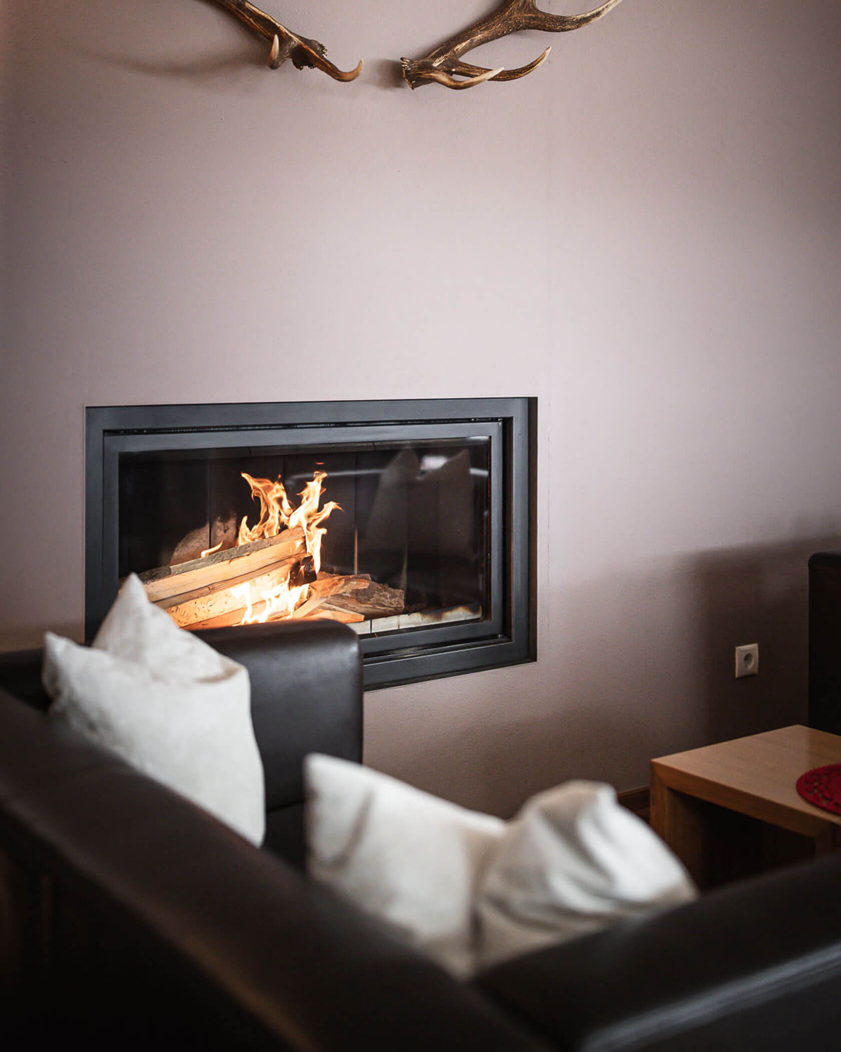 Geweih oberhalb vom Ofen, mit schwarzem Sofa im Vordergrund - Hotel Mühlwald