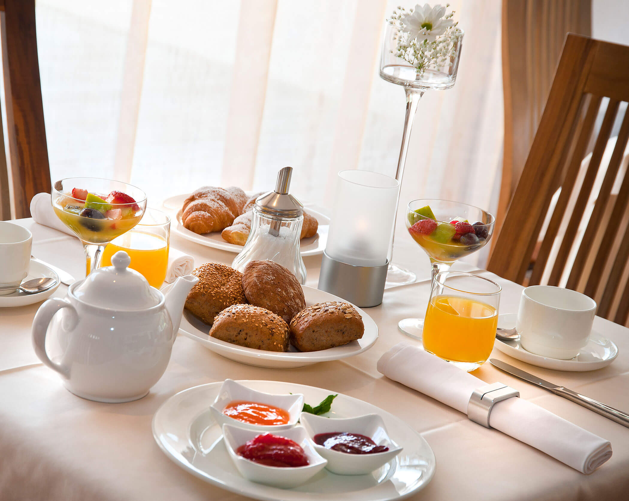 Gedeckter Frühstückstisch mit Broten, Obstsalat, Marmeladen, Saft und Croissants - Hotel Mühlwald